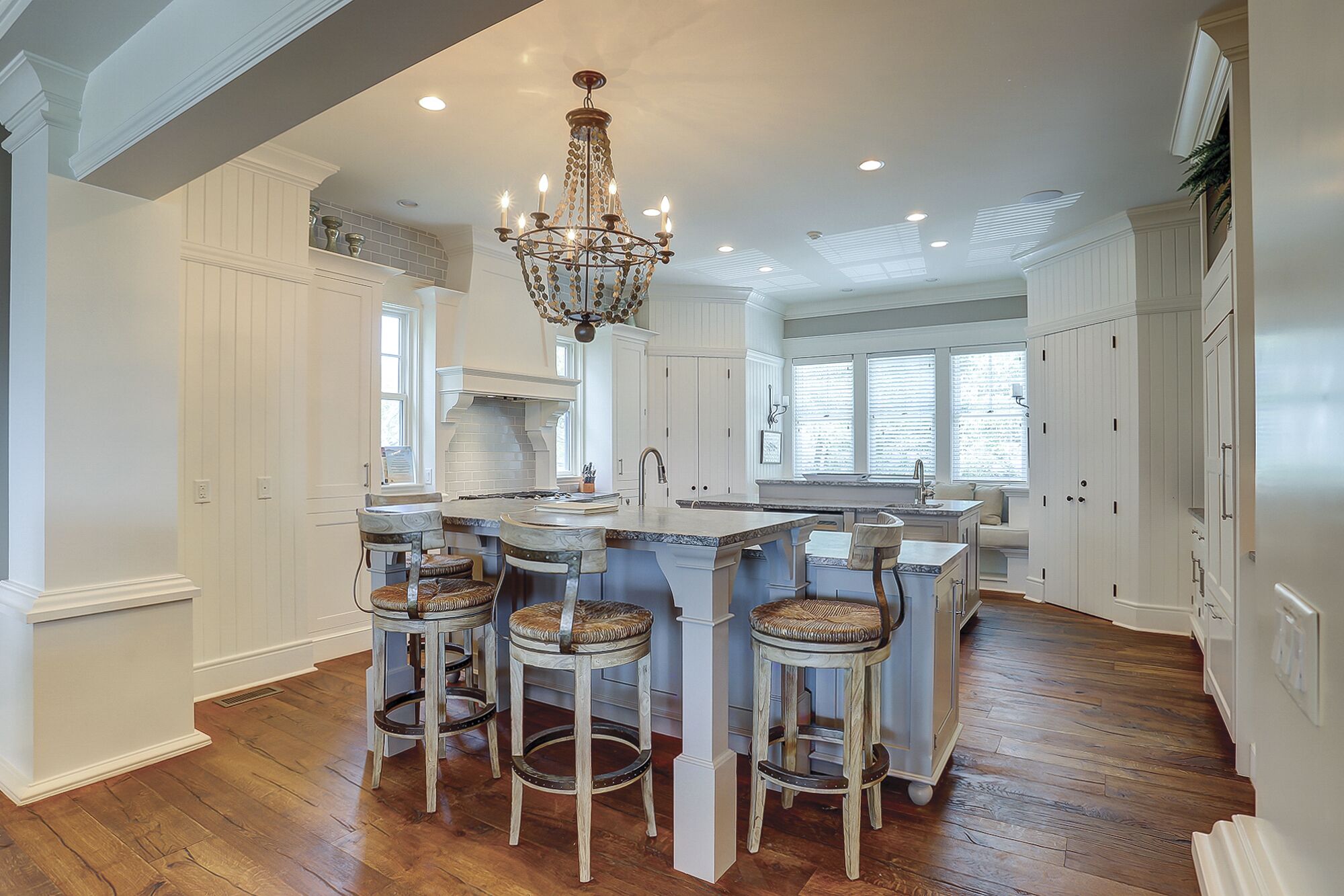 A spacious kitchen with white cabinetry, a central island with bar stools, a chandelier, and a large window providing natural light.
