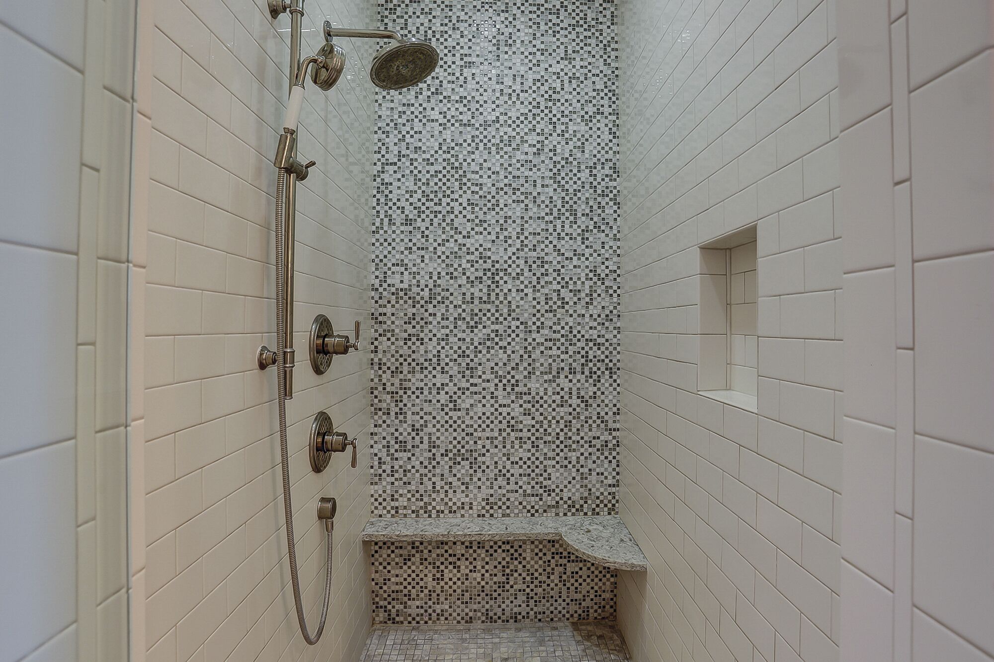 A narrow shower area with white tiled walls and a mosaic tile pattern on the shower wall.