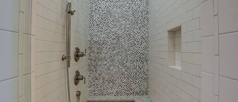 A narrow shower area with white tiled walls and a mosaic tile pattern on the shower wall.