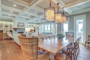 A spacious dining area with a large wooden table and wicker chairs, a built-in island with seating, and pendant lighting. - 31B Dune Lane - Coastal Chic Oceanfront 6-Bedroom Home! (Hilton Head Island)