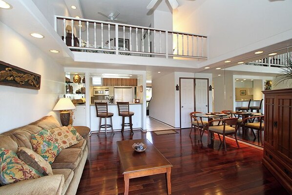 A spacious living area with a high ceiling, a dining table with chairs, a sofa, and a staircase leading to an upper level.