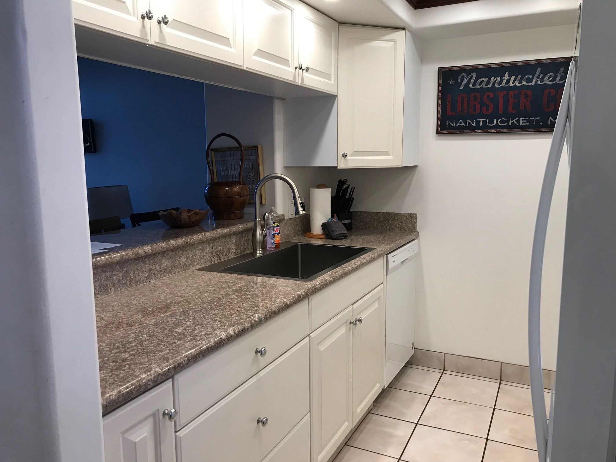 A kitchen with white cabinets, a granite countertop, a sink, and a sign on the wall advertising a lobster company.