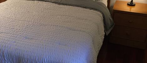 A neatly made bed with a grey quilt, multiple pillows including one with 'amour' written on it, and two bedside lamps on wooden nightstands.