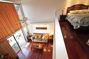 A bedroom with a wooden bed, a sofa, a ceiling fan, and a view of the outdoors through a sliding door.