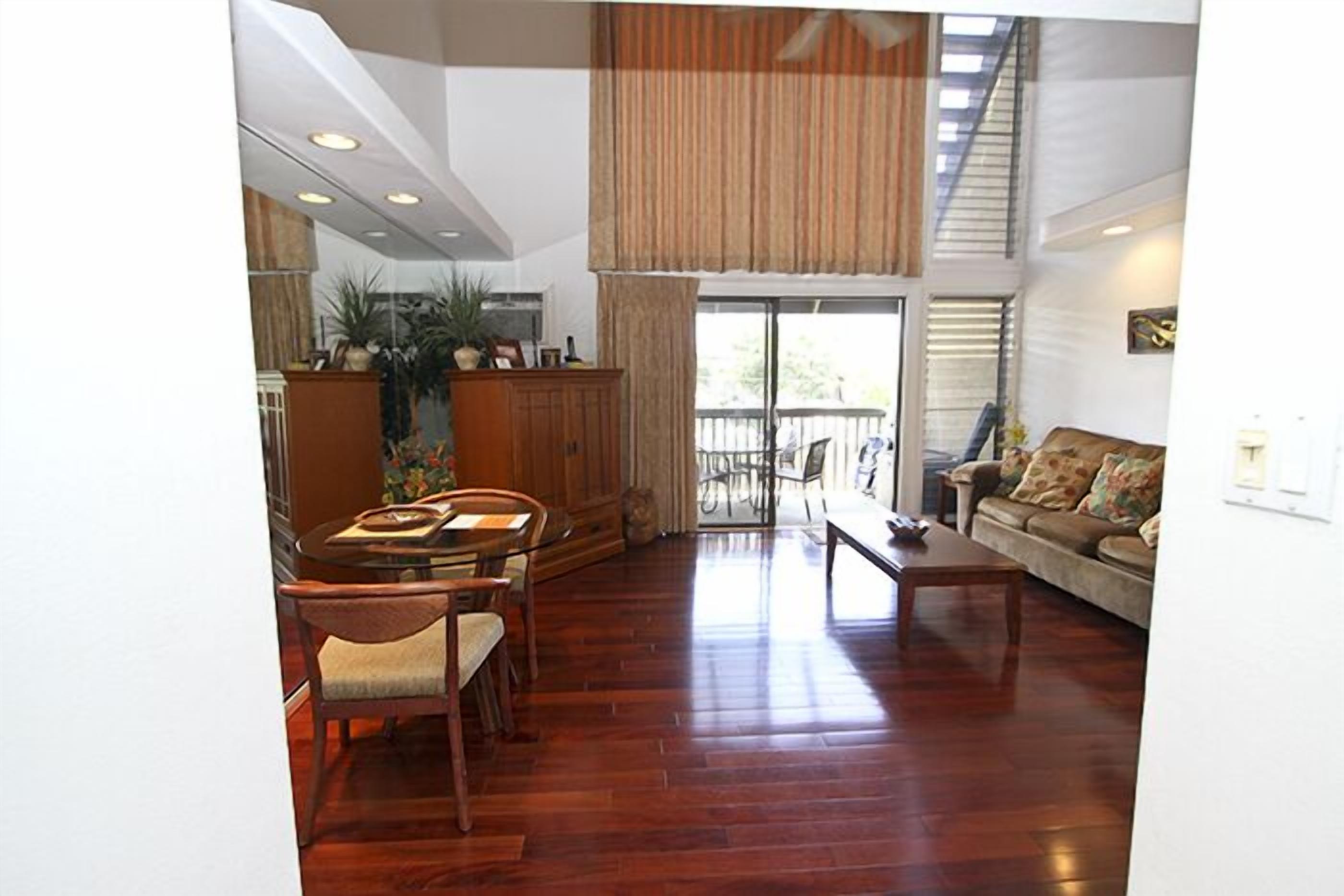 A spacious living area with a dining table and chairs, a sofa, and a large window with curtains.