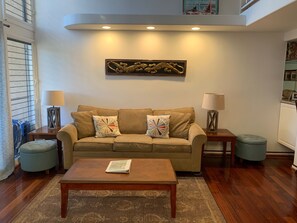 Un salon avec un canapé beige, deux poufs assortis, une table basse en bois et un élément décoratif mural.