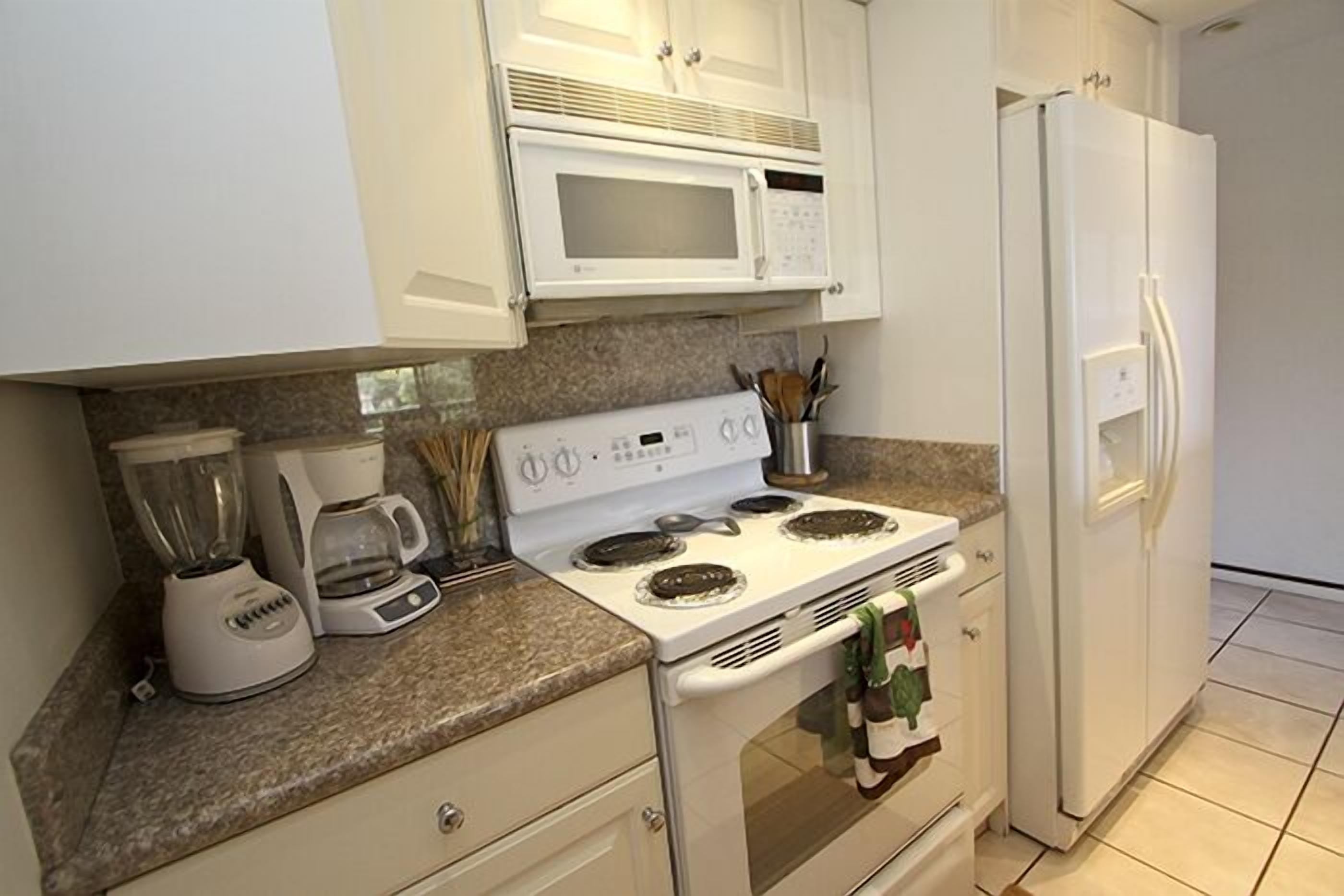 A kitchen with white cabinets, a microwave, a stove, a refrigerator, and a coffee maker.