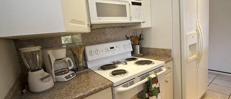 A kitchen with white cabinets, a microwave, a stove, a refrigerator, and a coffee maker.