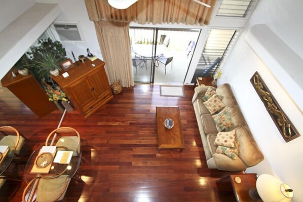 A spacious living area with a wooden floor, a sofa with patterned cushions, a coffee table, and a dining area with chairs and a table.