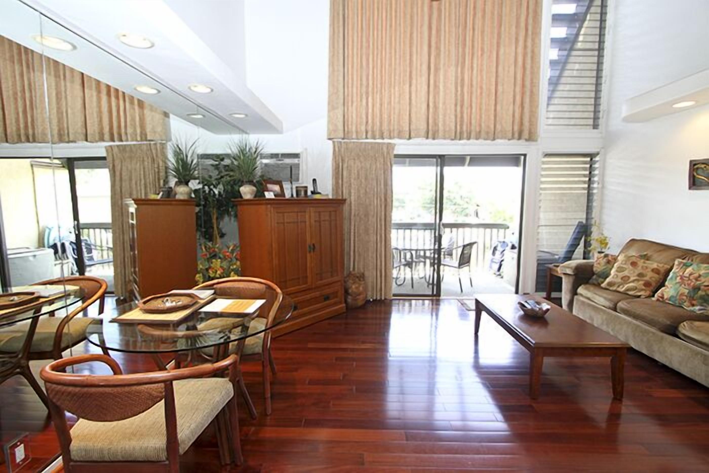 A spacious living room with a glass dining table, wooden chairs, a sofa, and a coffee table.