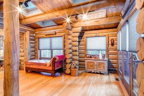 L'intérieur d'une cabane en rondins, avec un lit, une cheminée et une fenêtre.