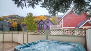 A hot tub in a backyard with a wooden fence, surrounded by colorful houses and a mountainous backdrop.
