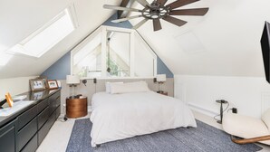 A bedroom with a sloped ceiling, a ceiling fan, a bed, a dresser, a chair, and a window.