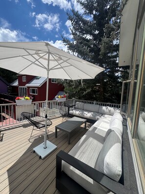 A deck with a white umbrella, outdoor furniture, and a flower planter.