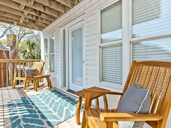 A covered porch with wooden furniture, a patterned rug, and a view of a house with white siding and a garage door.