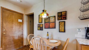 Un coin repas avec une table en bois, des chaises, une bouteille de vin et des œuvres d’art encadrées accrochées au mur.