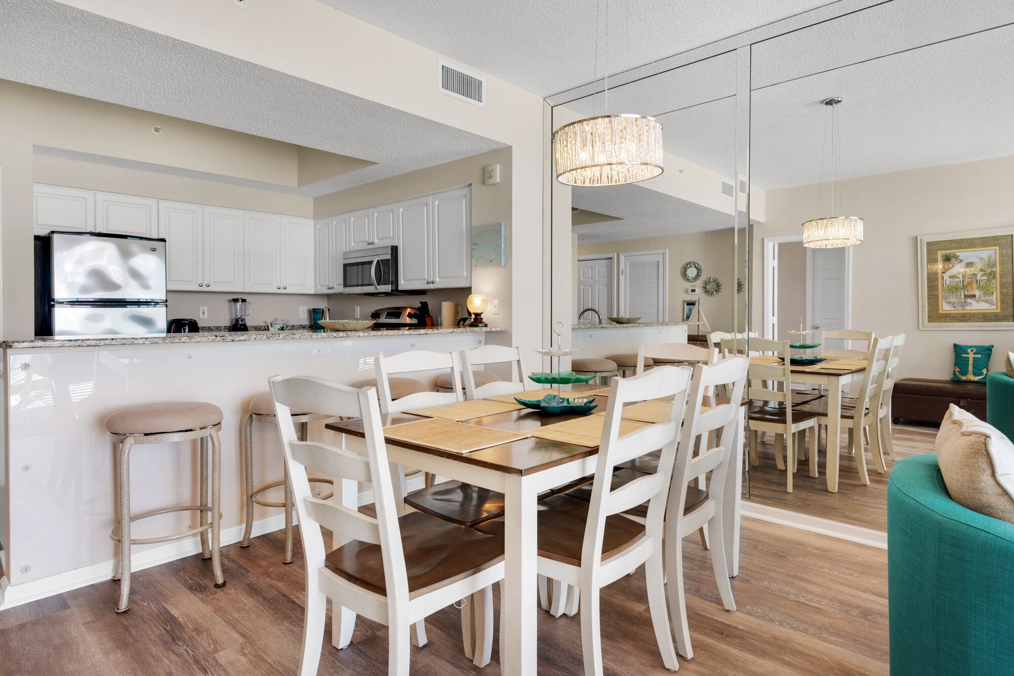 A modern kitchen with white cabinetry, a central island, and a dining area with white chairs and a wooden table.