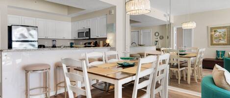 A modern kitchen with white cabinetry, a central island, and a dining area with white chairs and a wooden table.