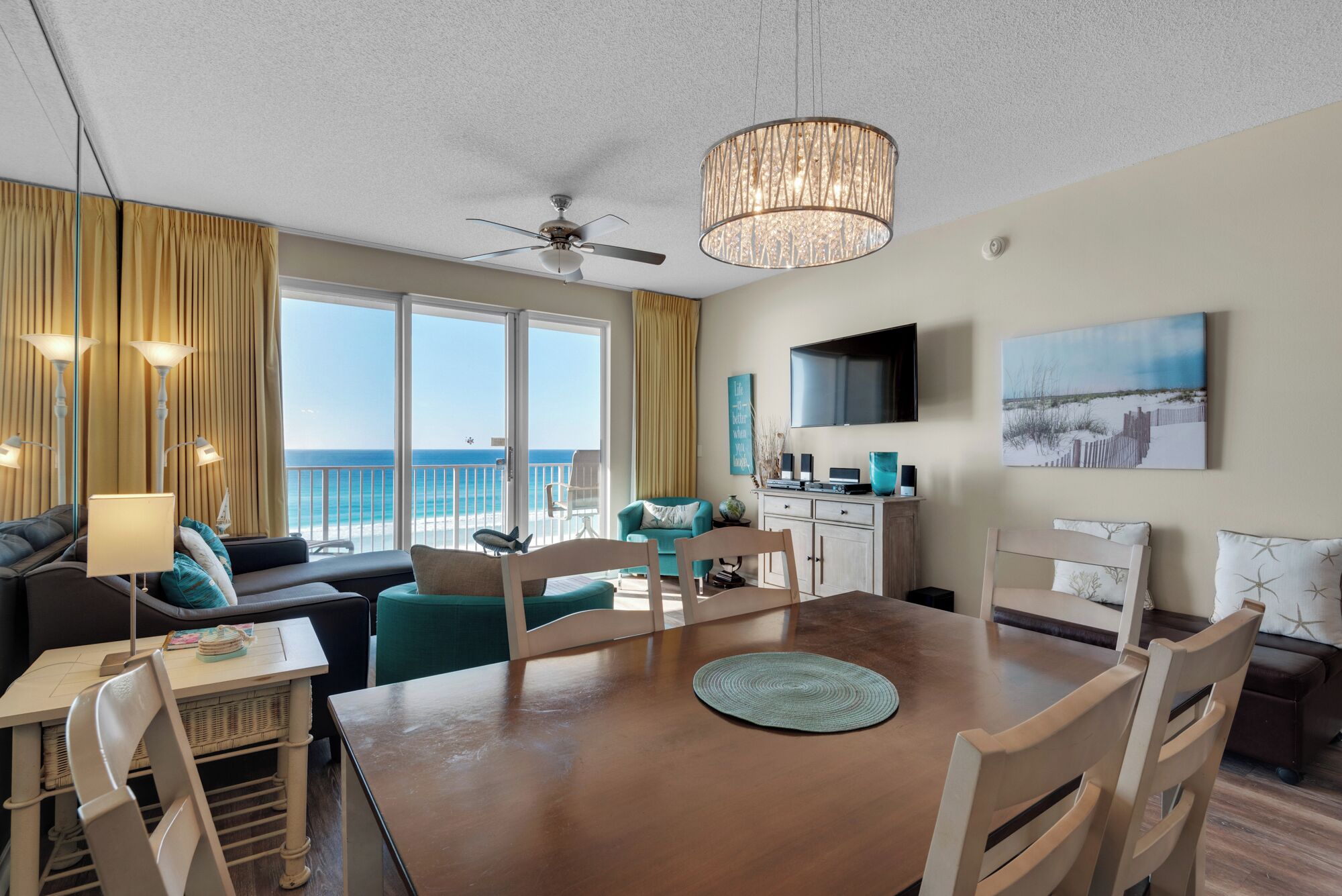 A spacious living area with a view of the ocean, a dining table, and a ceiling fan.