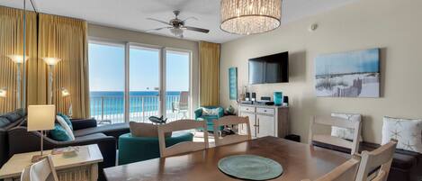 A spacious living area with a view of the ocean, a dining table, and a ceiling fan.