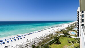 Blick auf einen Strand vom Balkon eines Hotels, mit Pool und Liegestühlen.