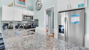 Eine moderne Küche mit weißen Schränken, einem Edelstahlkühlschrank, einer Mikrowelle und einem Waschbecken mit einer Granitabdeckung.