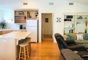 A compact living space with a kitchenette, a dining area with stools, a sofa, and a bookshelf.