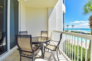 A balcony with a table and chairs, overlooking a beach and pool area. - Tommy Bahama themed beachfront condo w/private balcony! (Destin)