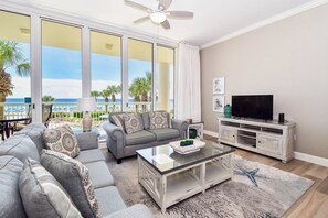 Een woonkamer met een bank, salontafel en tv-meubel, met een balkon en uitzicht op het strand.