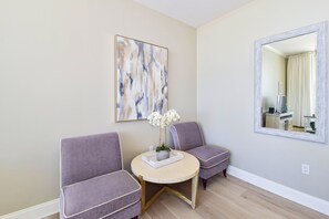 A room with a round table, two chairs, a painting, and a mirror.