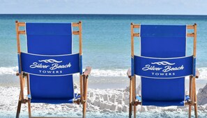 Twee strandstoelen met de branding "Silver Beach Towers" op een strand met een helder uitzicht op de oceaan.