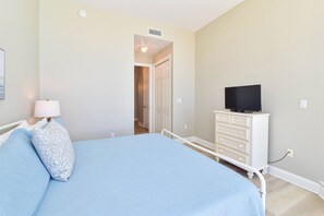 A bedroom with a bed, a dresser, a television, and a door leading to another room. - Tommy Bahama themed beachfront condo w/private balcony! (Destin)