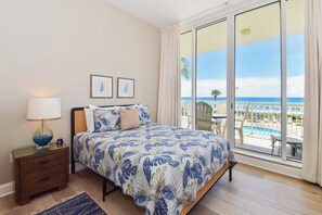 Une chambre avec un lit, une table de chevet, une lampe et une vue sur une piscine et une plage.