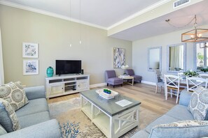 A living room with a flat-screen TV, two armchairs, a coffee table, and a dining area with a table and chairs. - Tommy Bahama themed beachfront condo w/private balcony! (Destin)