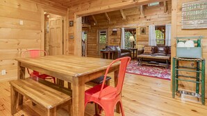 A wooden interior with a dining table, red chairs, a sofa, and a pet feeding station.