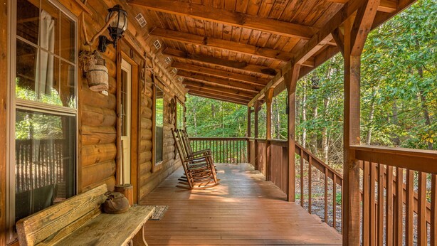 A wooden cabin with a porch, a bench, and rocking chairs.