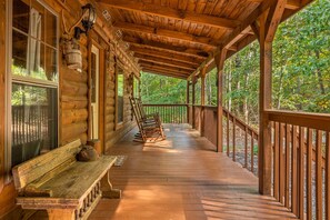 Une cabane en bois avec une véranda, un banc et des fauteuils à bascule.