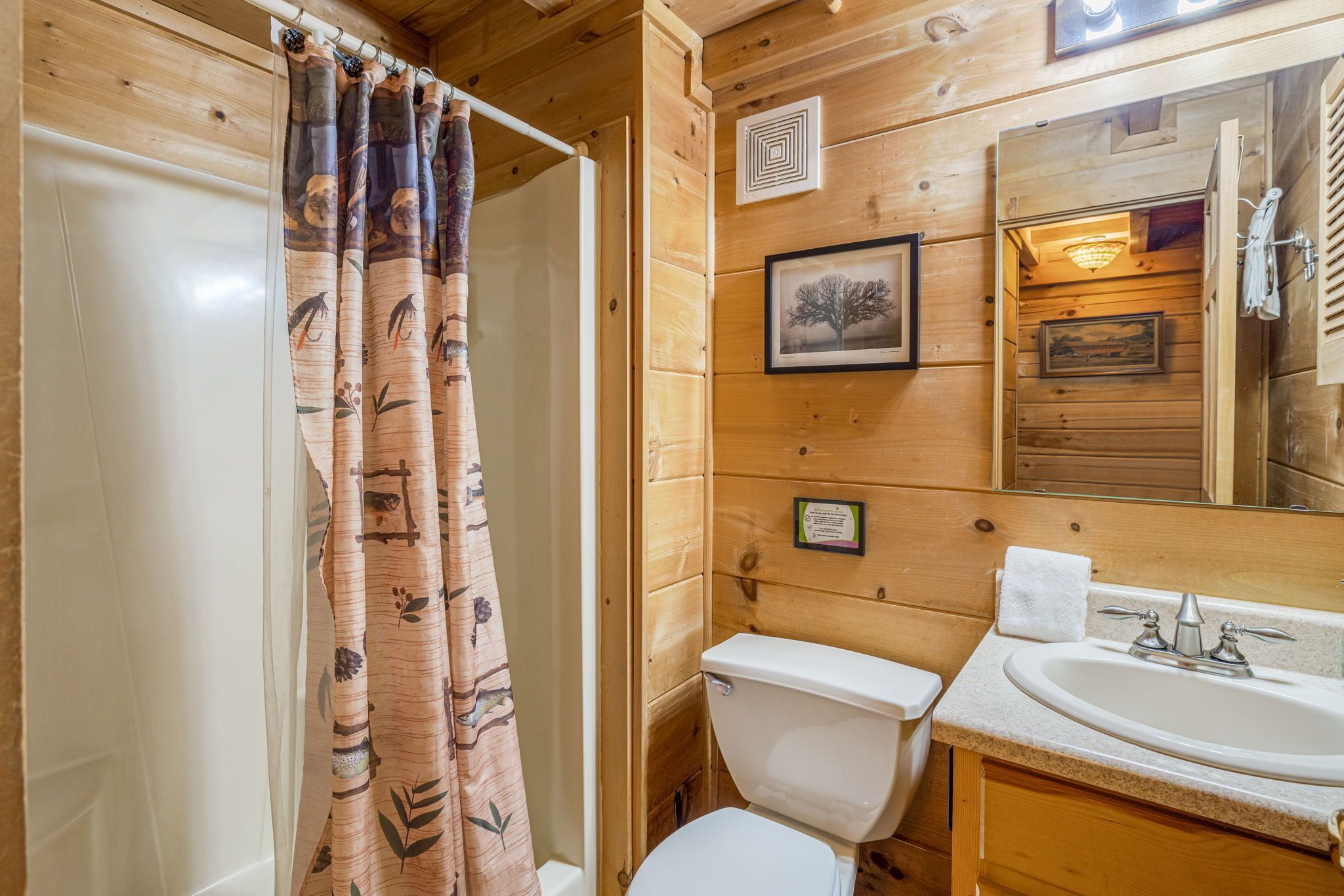 A wooden cabin bathroom with a shower curtain, toilet, sink, and a framed picture on the wall.