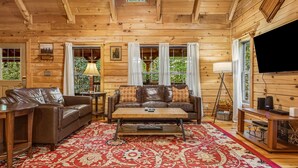 A wooden cabin interior with a leather sofa, a coffee table, and a red patterned rug.