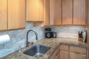 A kitchen with wooden cabinets, a granite countertop, a stainless steel sink, a coffee maker, and a toaster.