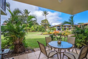 A patio with a round table and chairs, surrounded by lush greenery and palm trees.