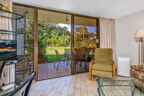 Een moderne woonkamer met een glazen deur die uitkomt op een terras met buitenmeubilair en uitzicht op een tuin.