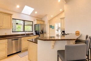 A modern kitchen with a central island, stainless steel appliances, and a large window.