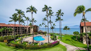 Un resort con piscina rodeada de palmeras, campo de golf y vistas al océano.