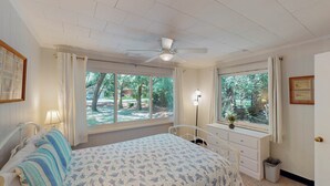 A bedroom with a bed, a desk, a chair, a ceiling fan, and large windows with curtains. - Bradfield 4 bedrooms, 2.5 bathrooms (Jekyll Island)