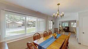 A dining room with a long wooden table, chairs, a chandelier, and large windows with blinds. - Bradfield 4 bedrooms, 2.5 bathrooms (Jekyll Island)