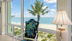 A room with a large window offering a view of a beach and palm tree.