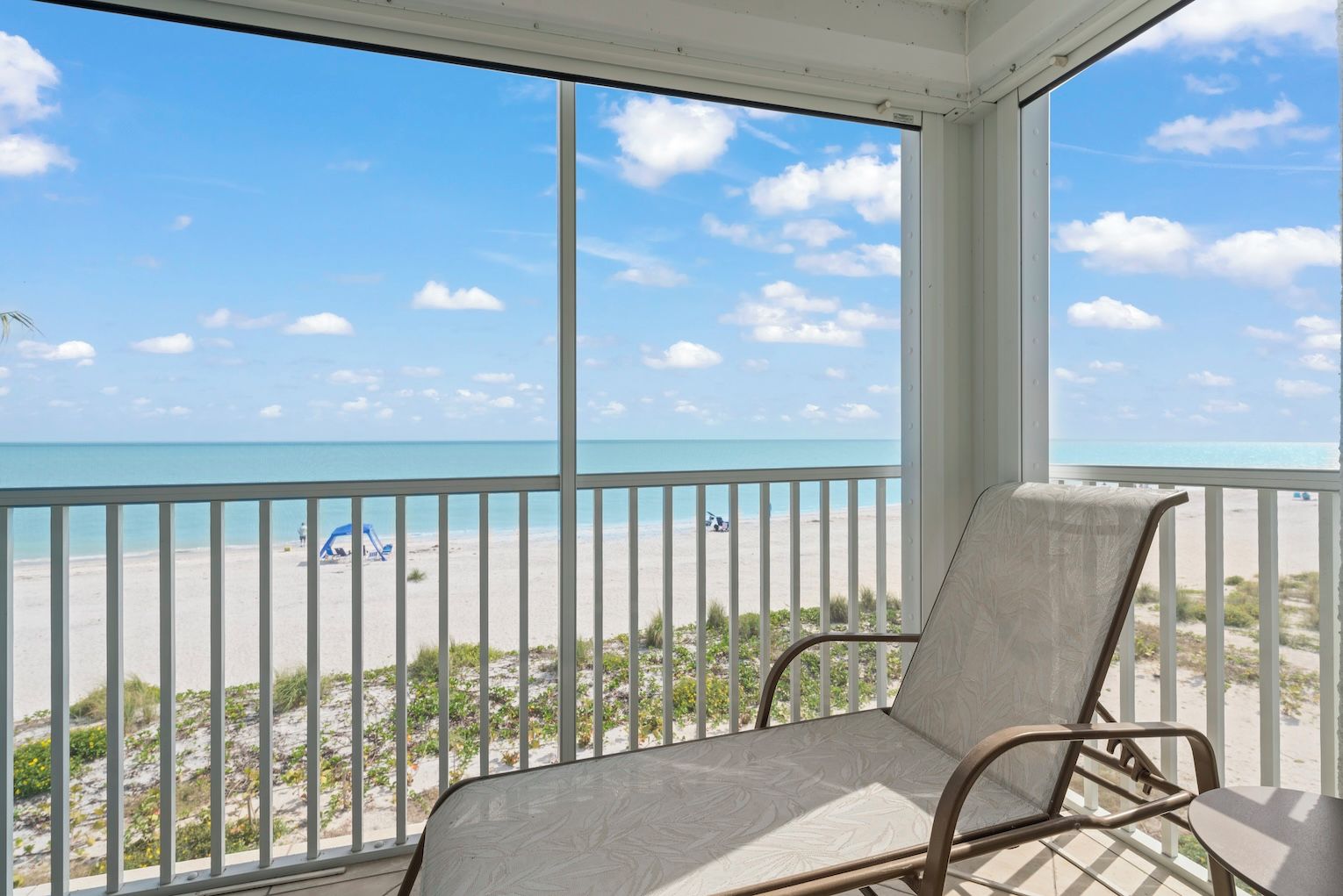 Uma varanda com vista para a praia, uma cadeira e uma mesa.
