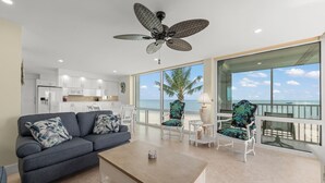 A modern living room with a sofa, coffee table, and chairs, a ceiling fan, and a view of the ocean.