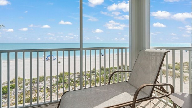 A balcony with a view of a beach, a chair, and a table.